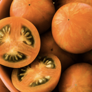 A close-up of orange tomatoes, one sliced open showing green seeds.